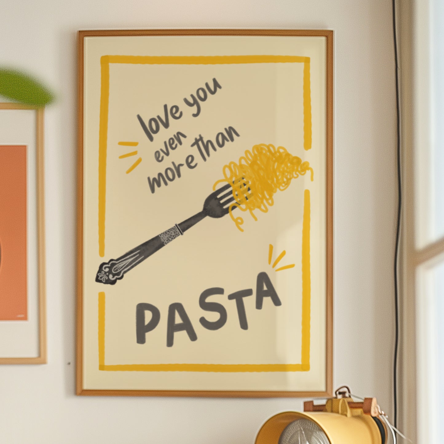 A framed kitchen art print on a beige wall, featuring a yellow border, the phrase 'love you even more than PASTA' in dark gray lettering, and a black fork holding yellow spaghetti noodles.