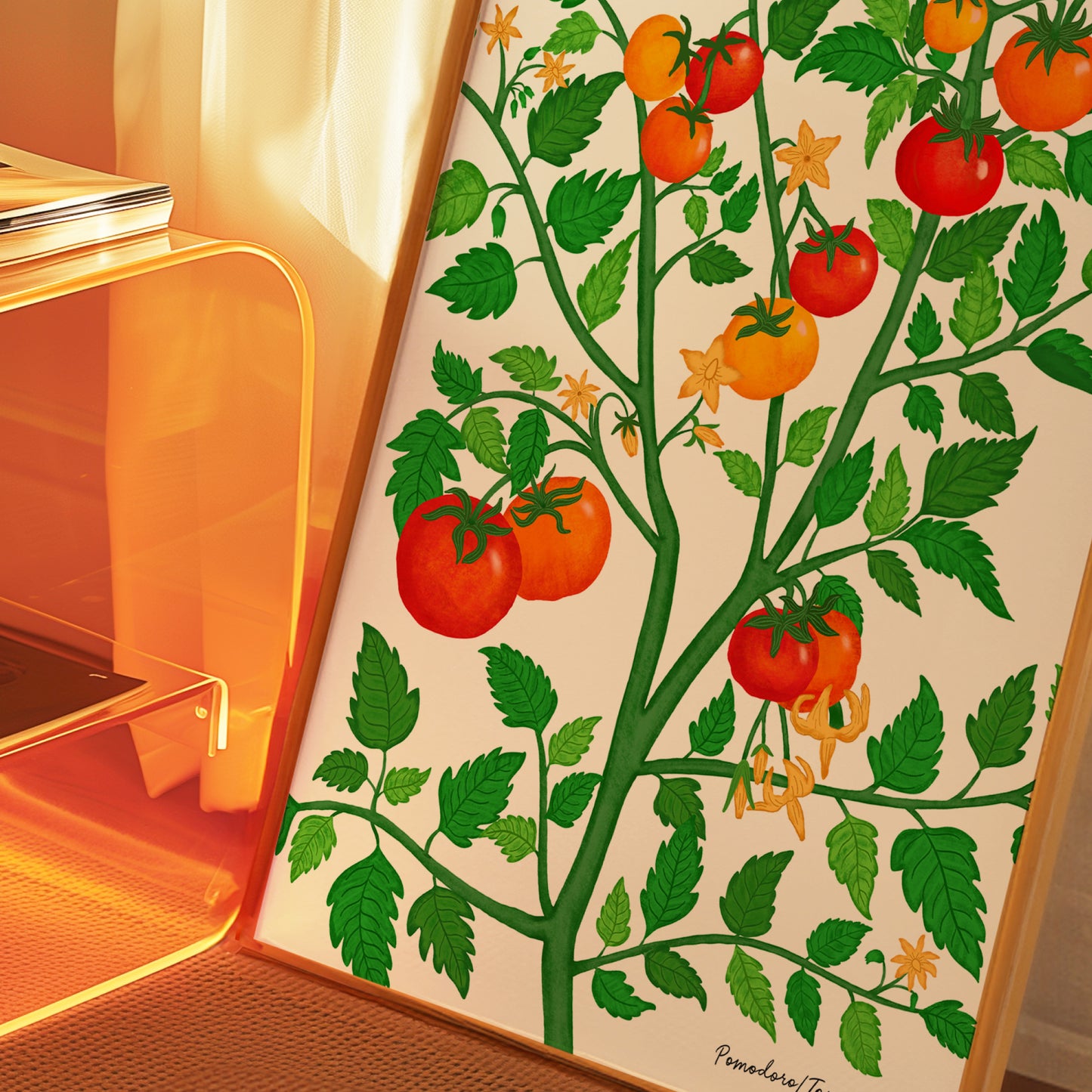 A framed botanical art print of a tomato plant with green leaves and red and orange tomatoes, leaning against a glass side table in warm, orange-toned ambient light.