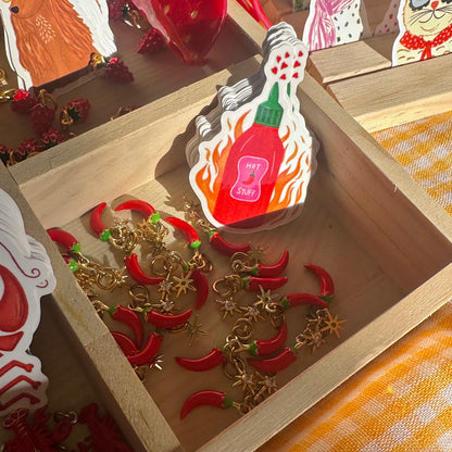 Decorative item with red peppers and gold chains in a wooden box, surrounded by other decorative items.