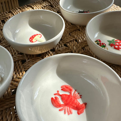 Set of white bowls with red crab designs on a woven surface
