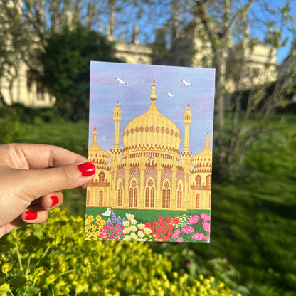 Hand holding a postcard with a colorful illustration of a building in a garden setting
