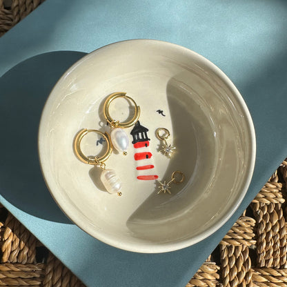 Jewelry dish with lighthouse-themed earrings on a textured surface