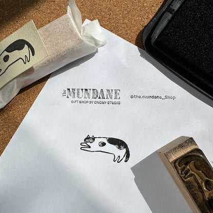 Stylized cat stamp on a piece of paper with 'The Mundane' branding.