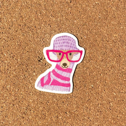 Sticker of a dog wearing a pink sweater and glasses on a cork background
