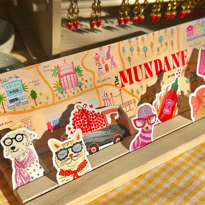 Collection of small figurines and decorative items on a wooden shelf with 'The Mundane' branding.
