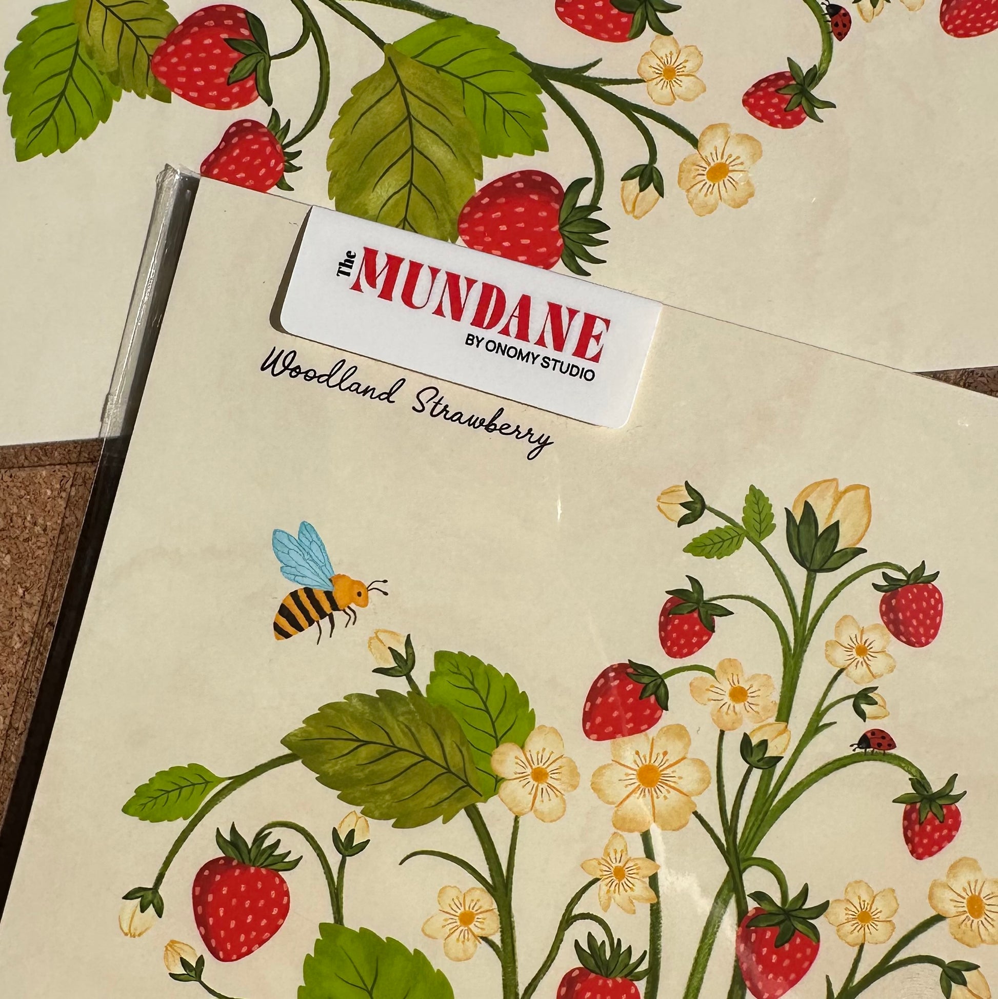 Notebook with strawberry and floral design and 'The Mundane' branding.