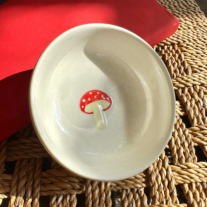 White ceramic dish with a red mushroom design on a woven mat