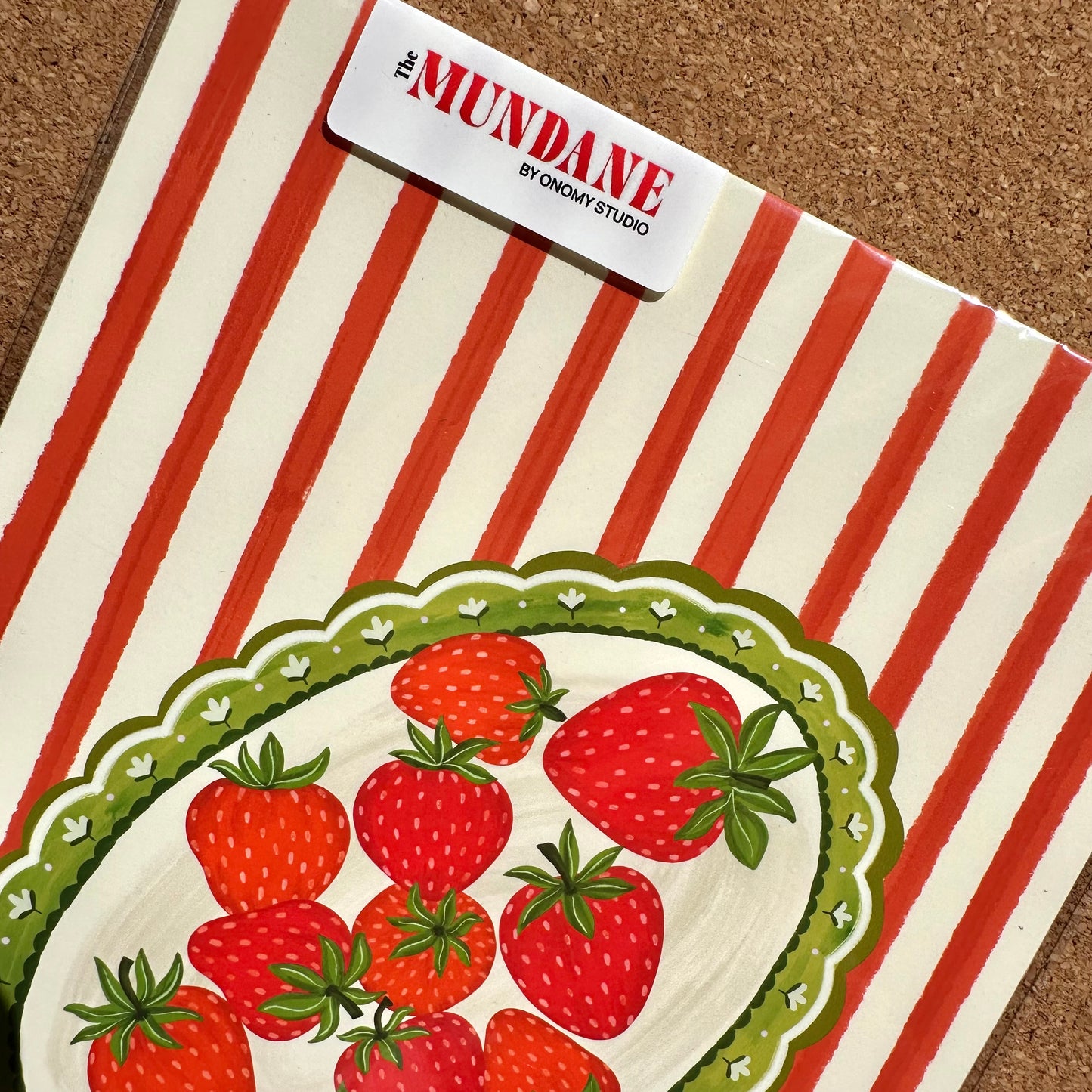 Book with red and white striped cover featuring strawberries on a brown surface