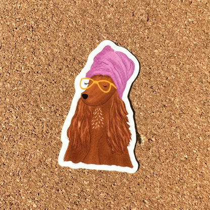 Sticker of a brown dog with a purple towel and yellow glasses on a cork background