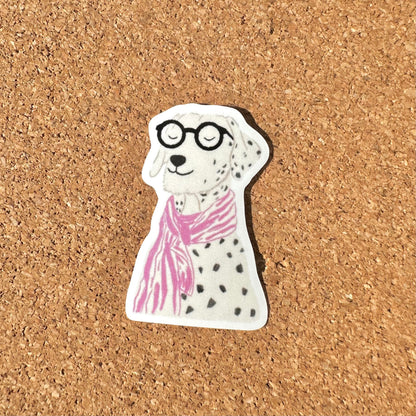Sticker of a dog wearing glasses and a pink scarf on a cork background
