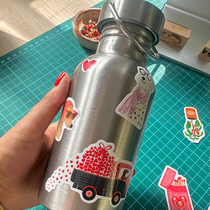 Silver water bottle with stickers held by a hand on a green cutting mat.