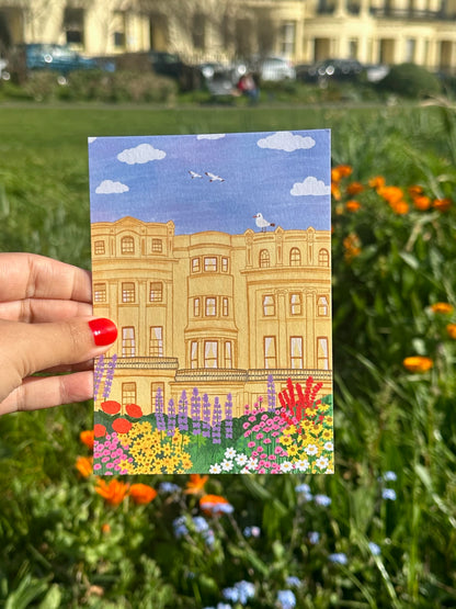 Hand holding a postcard with a building illustration in a garden setting