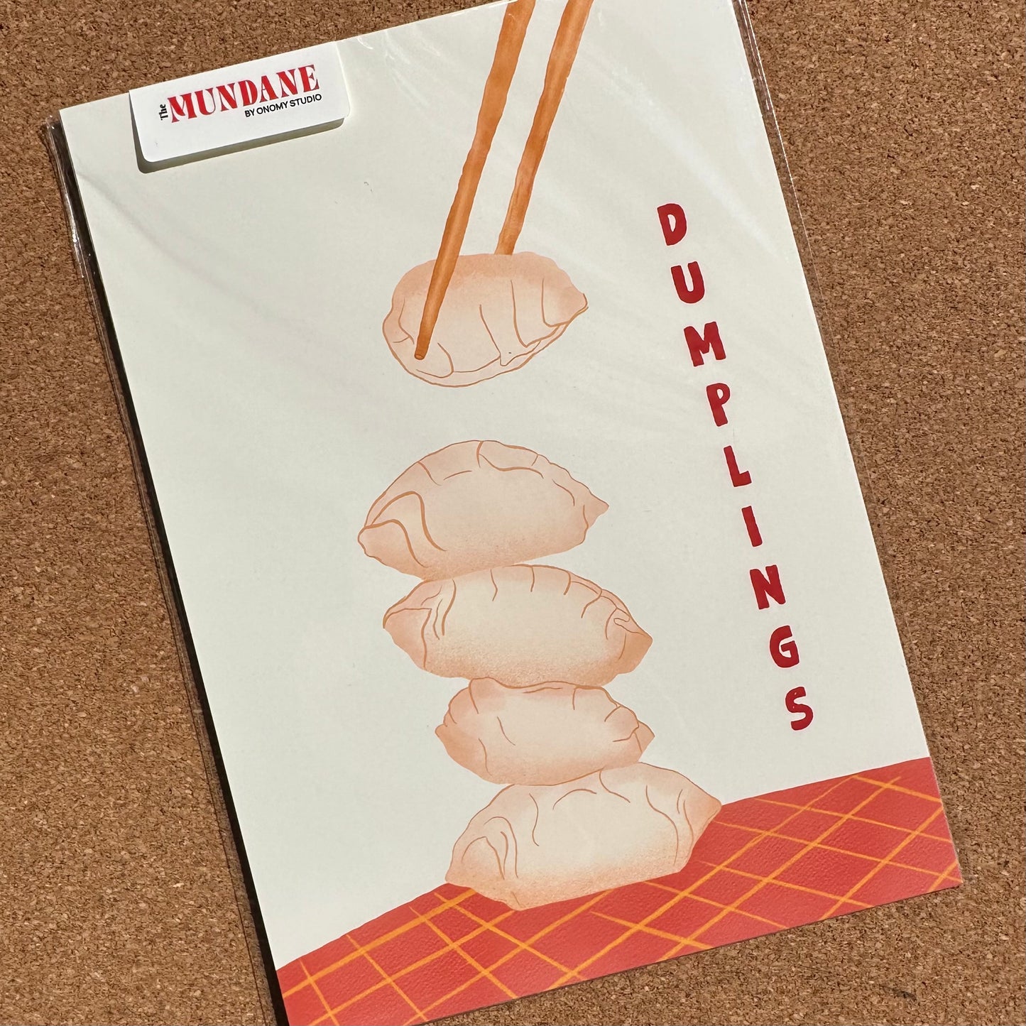 Notebook with dumplings illustration and 'The Mundane' branding on a textured surface