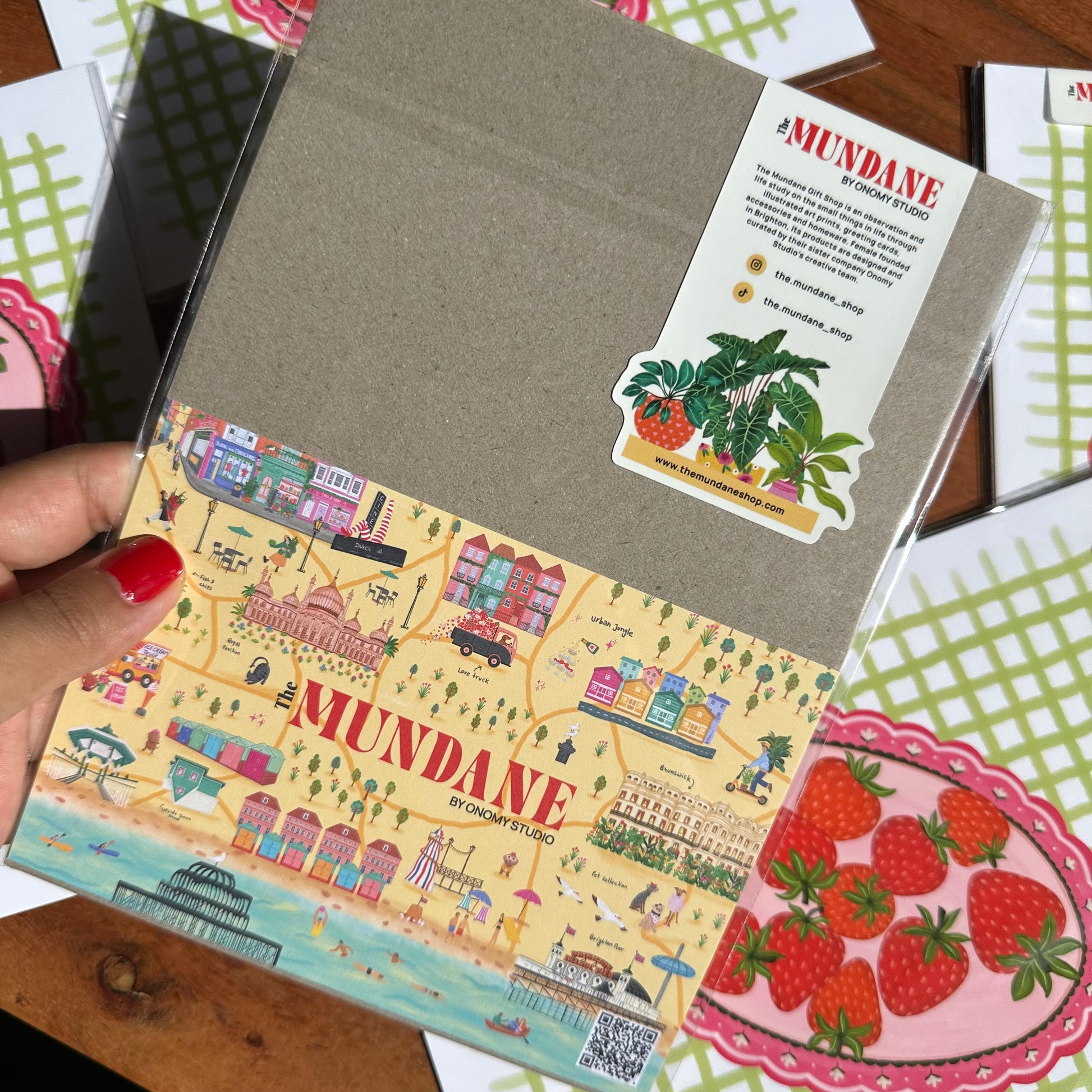 Notebook with 'Mundane' branding held by a hand, surrounded by other items on a wooden surface.