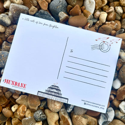 Postcard with 'The Mundane' branding on a bed of pebbles