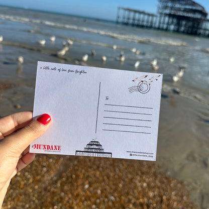 Hand holding a postcard with a beach and pier in the background