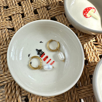 White ceramic bowl with gold hoop earrings on a woven mat