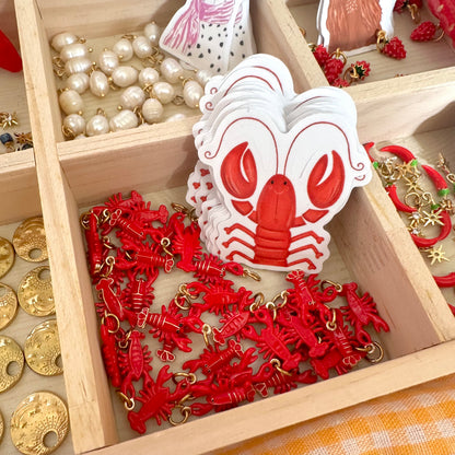 Red lobster-shaped figurines with gold accents in a wooden box.