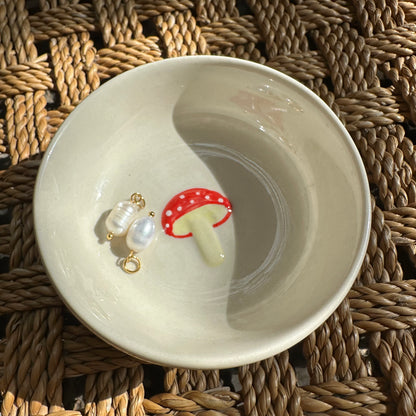 White ceramic dish with a red mushroom design on a woven surface