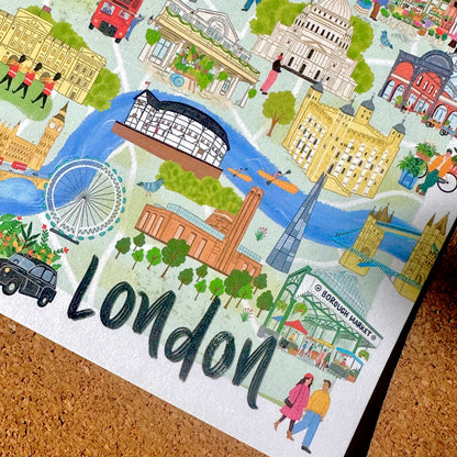 A close-up of a London-themed illustrated print or poster featuring landmarks such as Big Ben, the London Eye, Tower Bridge, St. Paul's Cathedral, and the word 'London' in large black script, placed on a cork surface.
