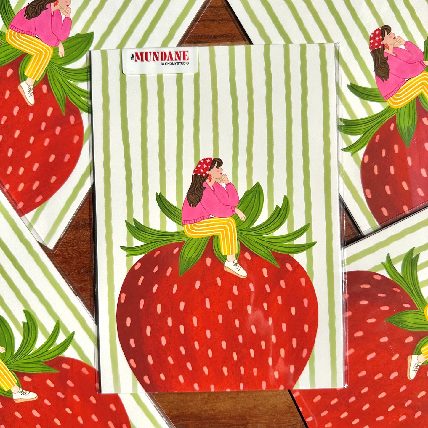 Illustration of a person sitting on a strawberry with a striped background, featuring the brand 'Mundane'.