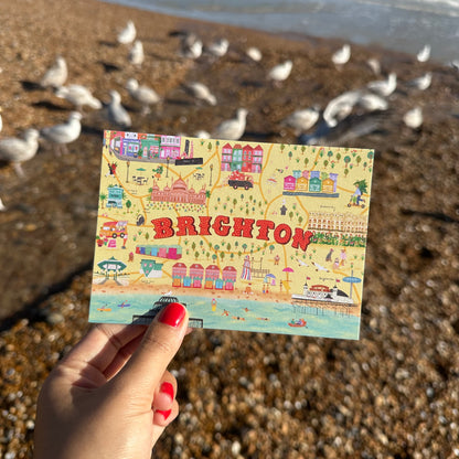 Hand holding a colorful map of Brighton on a beach with seagulls in the background