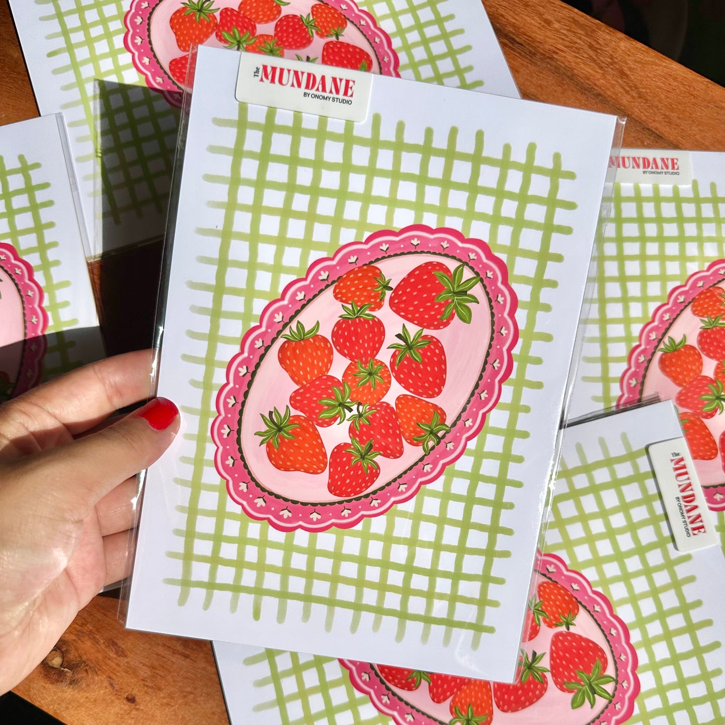 Strawberry-themed cards with green grid pattern held by a hand on a wooden surface.
