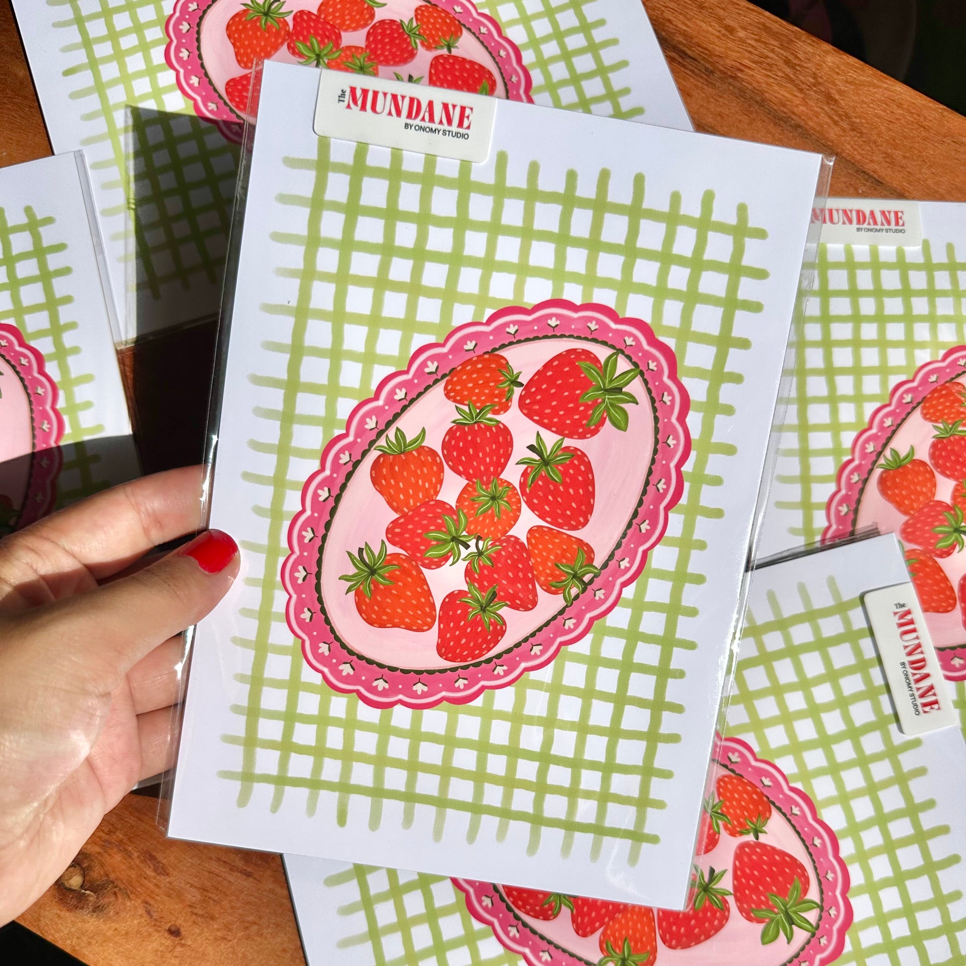 Strawberry-themed cards with green grid pattern held by a hand on a wooden surface.