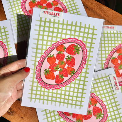 Strawberry-themed cards with green grid pattern held by a hand on a wooden surface.