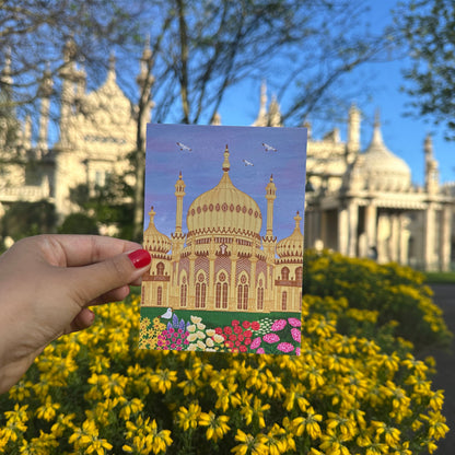 Hand holding a postcard with a colorful illustration of a building in front of a real-life architectural background.