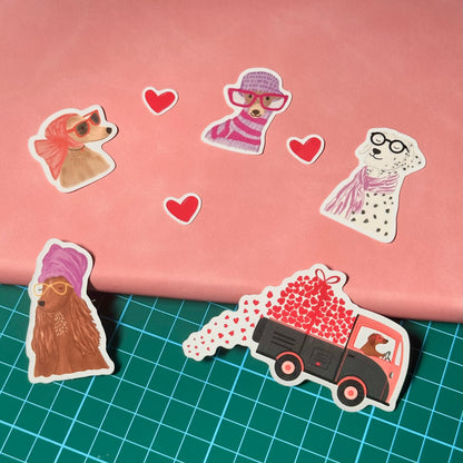 Stickers of dogs wearing scarves and sunglasses, hearts, and a truck with hearts on a pink and green grid background.