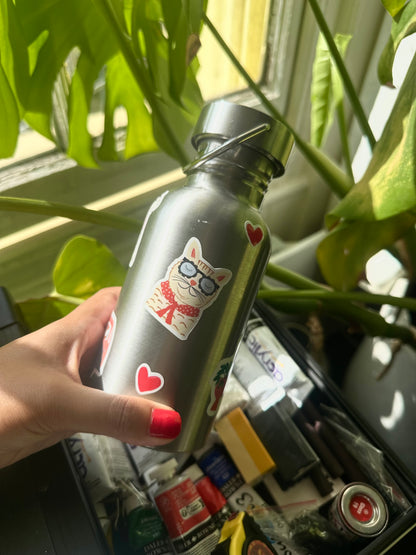 Person holding a silver water bottle with a cat design in front of green plants