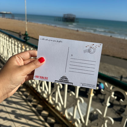 Hand holding a postcard with a beach and pier in the background