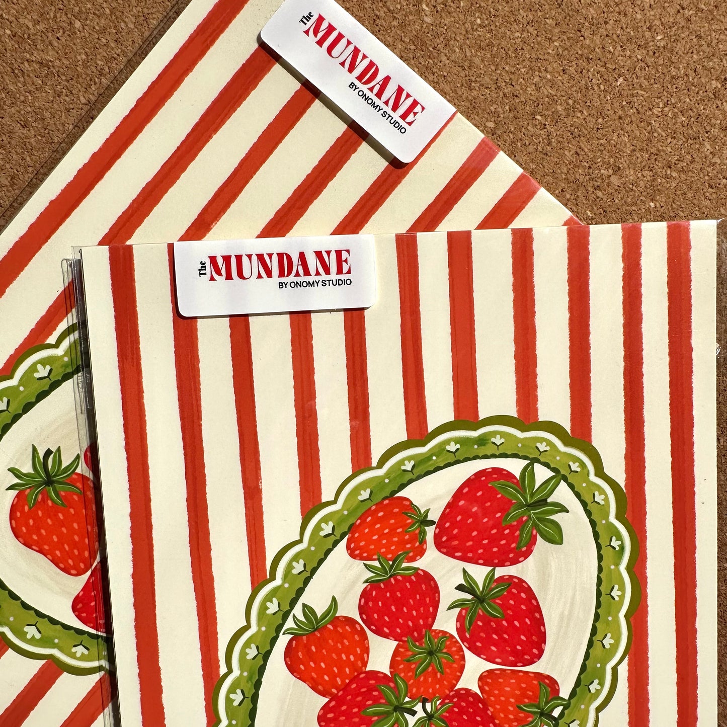 Two notebooks with strawberry design on a red and white striped background, branded 'Mundane'.