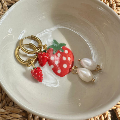 Strawberry-themed keychain with gold rings and pearl-like beads on a white ceramic dish.