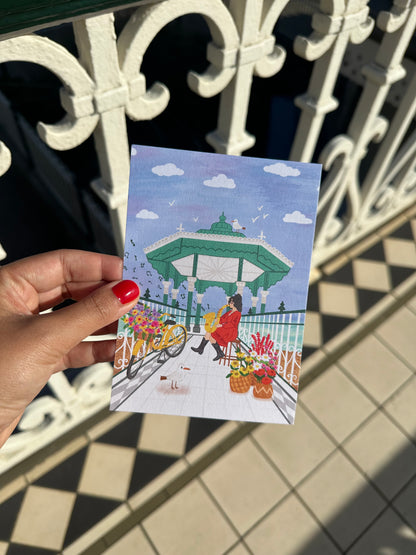 Hand holding a colorful postcard with a design of people by a pool against a tiled wall.