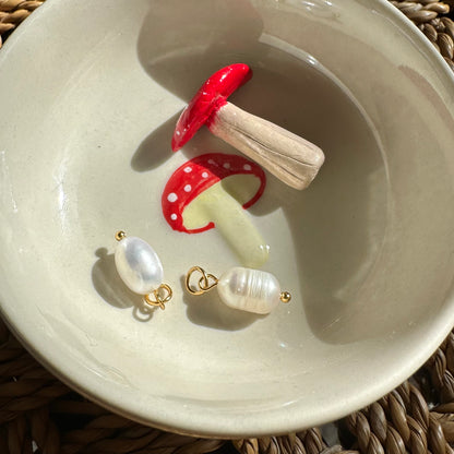 Decorative red mushroom with white spots and pearl earrings on a ceramic plate.