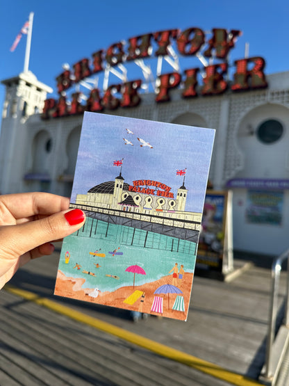Hand holding a postcard with a colorful illustration of a building against a blue sky, with a Ferris wheel and 'Coney Island' sign in the background.