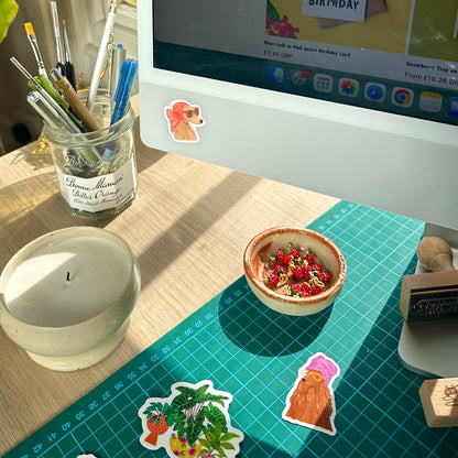 Desk setup with a computer, candle, and decorative items on a green cutting mat.