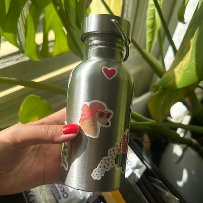 Silver water bottle with dog stickers held by a hand in front of green plants