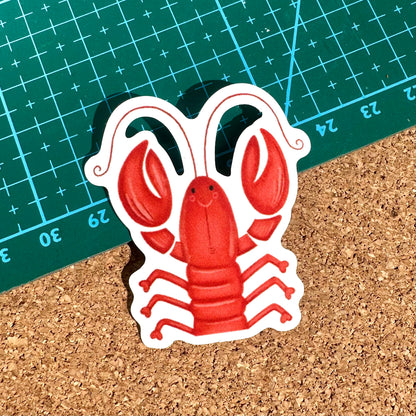 Sticker of a red lobster on a cork surface with a green cutting mat in the background