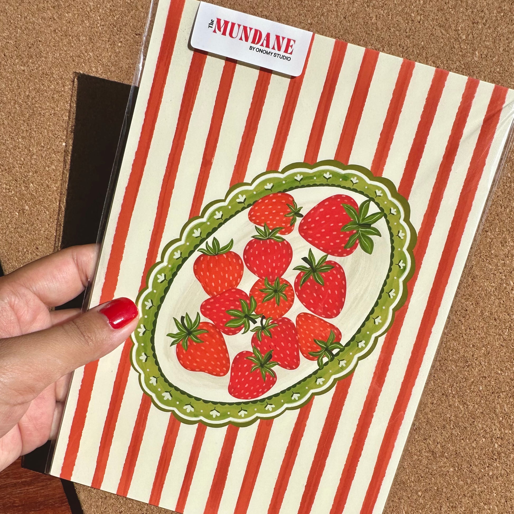 Notebook with red and white striped cover and strawberry design held by a hand.