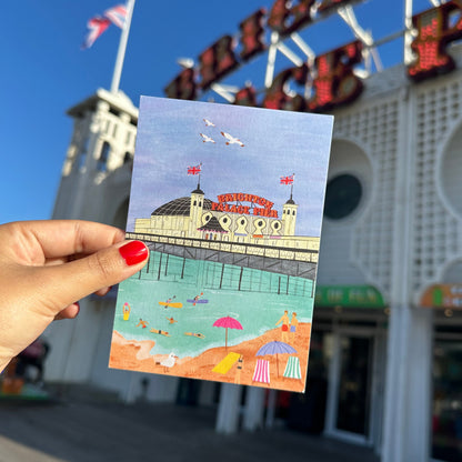 Hand holding a postcard with a beach scene in front of a building with a sign.