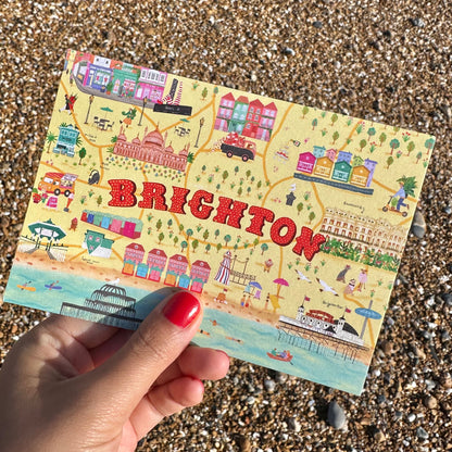 Colorful postcard of Brighton held by a hand on a pebble beach