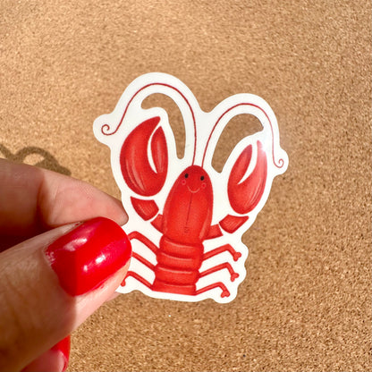 Red lobster sticker held by a hand with red nail polish on a beige background
