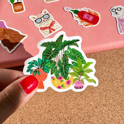 Hand holding a sticker of plants on a cork board with other stickers in the background.