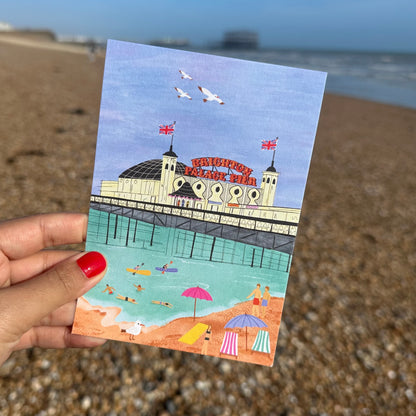 Illustrated postcard of a beach scene with a pier and people on a pebbly beach.