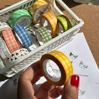 Basket of colorful washi tape with a hand holding a roll of yellow and white checkered tape.