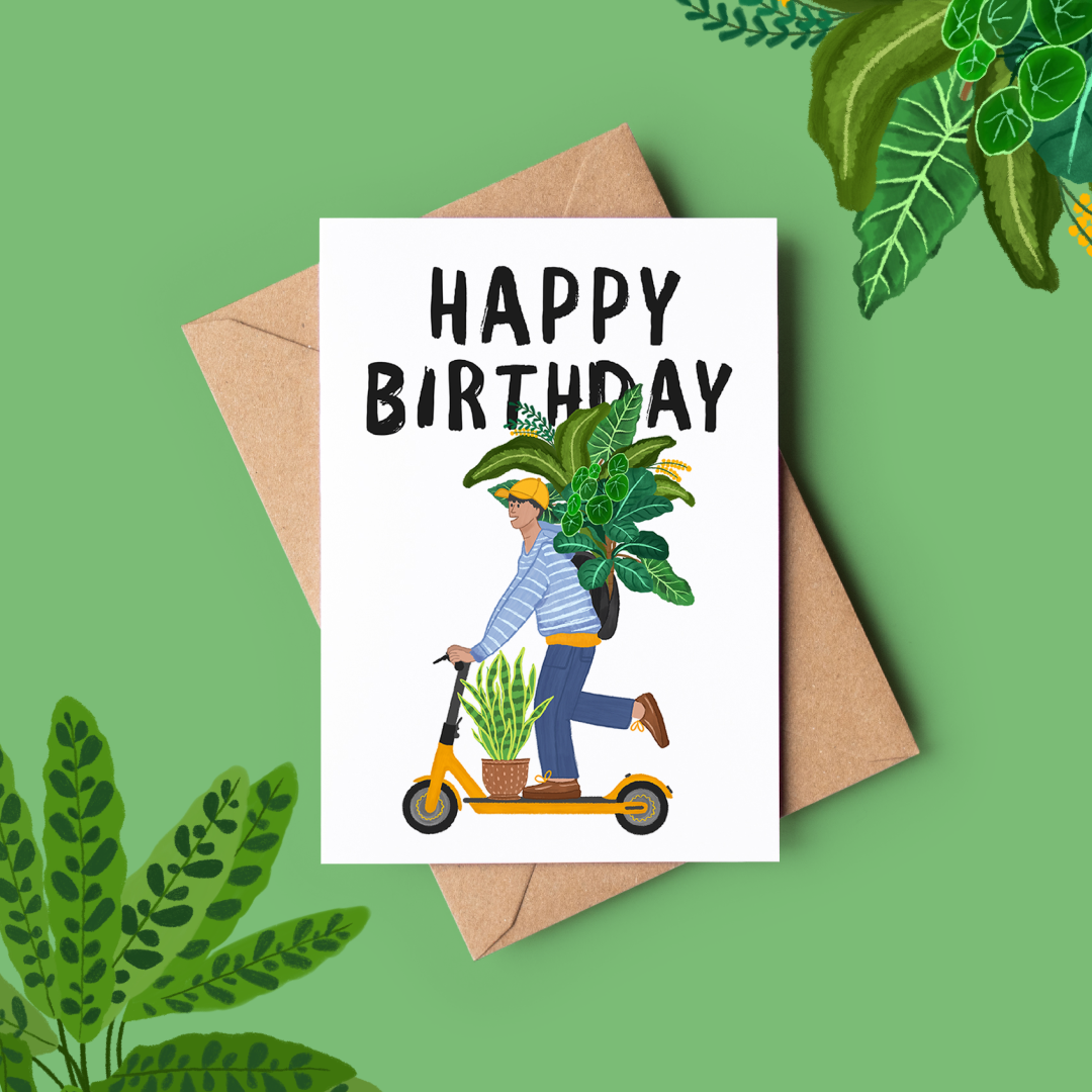 A greeting card with a hand-drawn illustration of an east London guy on a scooter carrying a large plant. The card reads 'HAPPY BIRTHDAY' and is placed on a green background with foliage around it.