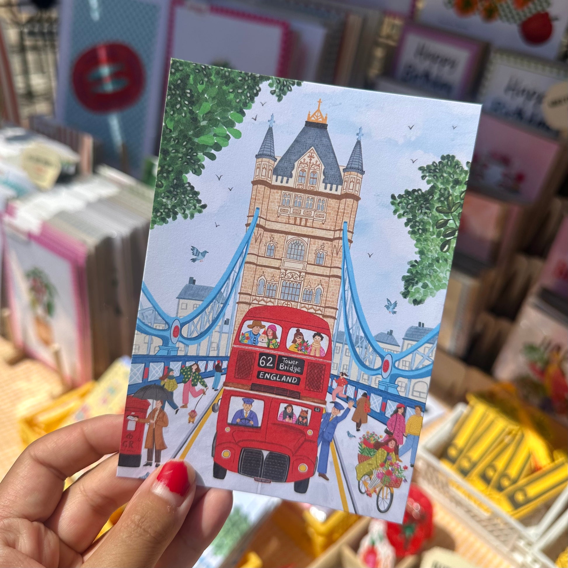 Illustrated Tower Bridge postcard showing red London bus, cyclists and cat in a jumper, London souvenir postcard by The Mundane Gift Shop